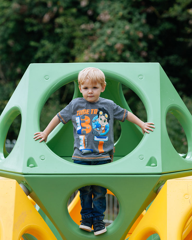 Un jeune garçon regarde à travers une structure de jeu en plastique playcubes qu'il a escaladée.